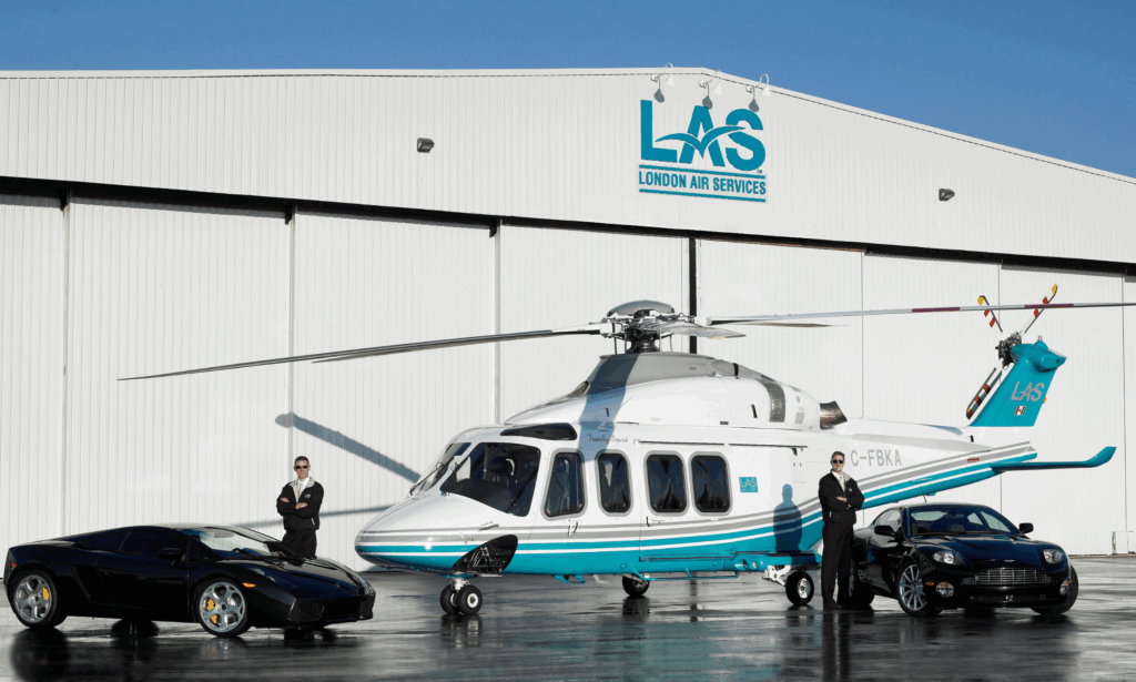 Two London Air Services pilots standing beside twin-engine AW139 helicopters and premium black luxury cards, highlighting executive-class travel and professional aviation service at Vancouver's YVR South Terminal.